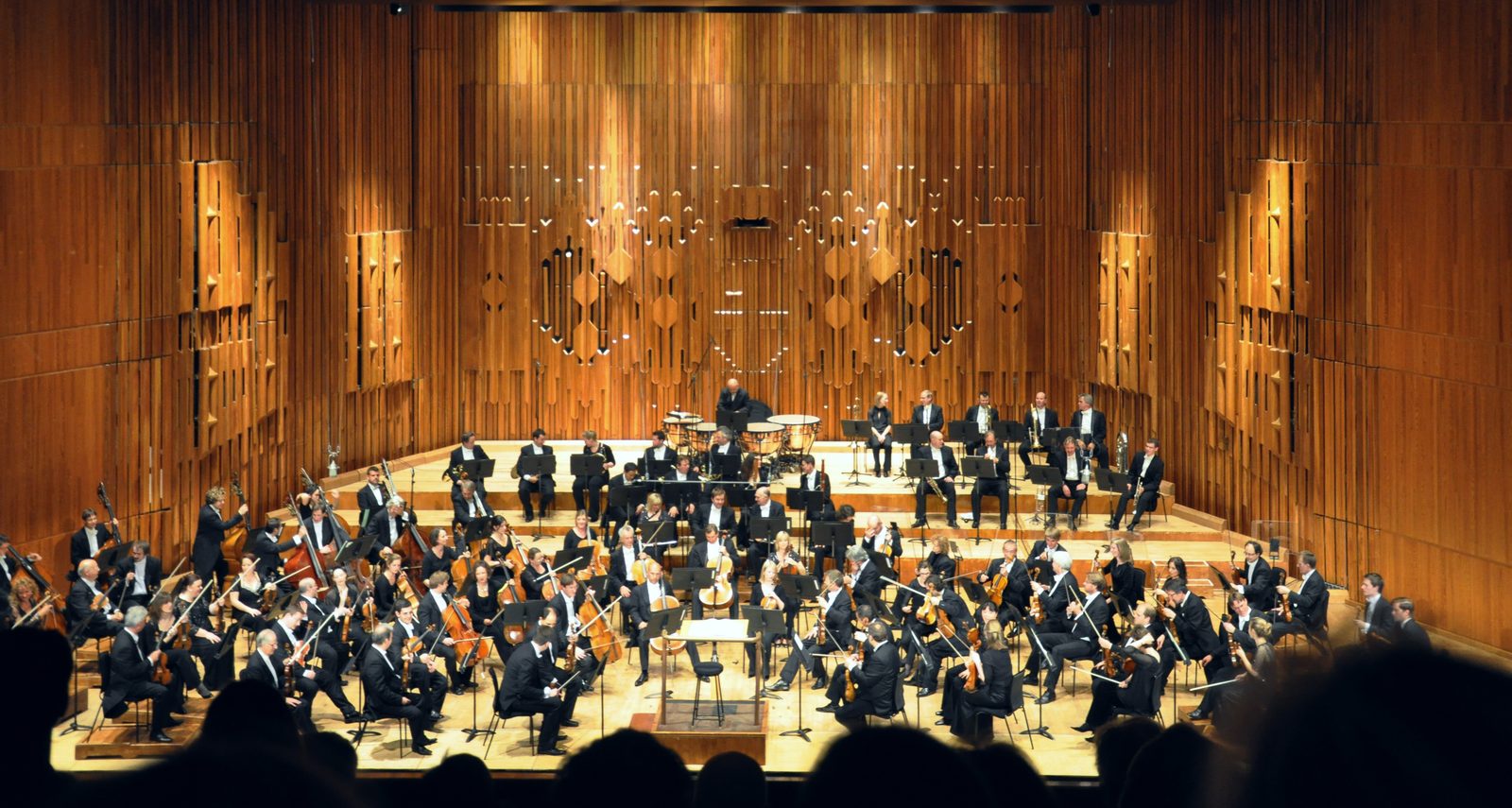 A symphony orchestra seen from the circle of a concert hall, on the centre line, looking down onto the players.